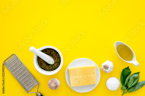 Make pesto sauce. Cheese  garlic  green basil  olive oil  salt near grater and mortar on yellow background top view copy space