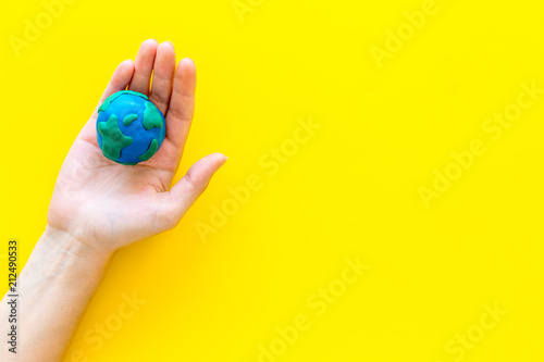 Fototapeta Naklejka Na Ścianę i Meble -  Earth. Hand hold plastiline symbol of planet Earth globe on yellow background top view space for text