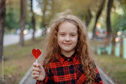 Sweet girl with a lollipop in a autumn park.