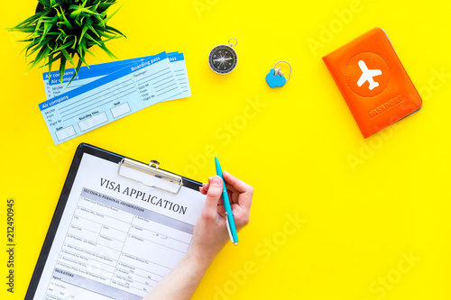 Hand fills visa application form. Form near glasses, pen, passport cover with airplane signand airplane tiskets on yellow background top view copy space photo