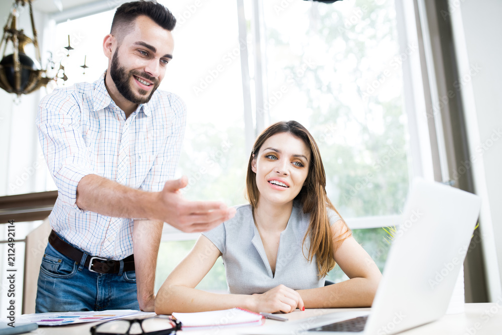 Low angle portrait of two modern business professionals discussing project pointing at laptop screen while working in office Low angle portrait of two modern business professionals discussing project pointing at laptop screen while working in office