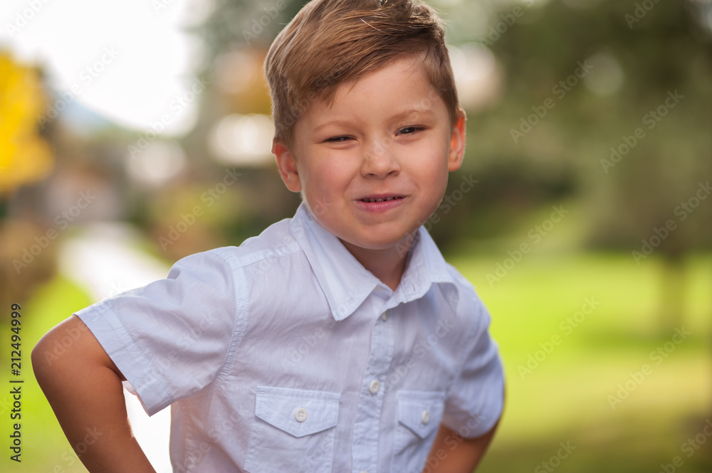 Portrait of funny cheerful positive boy in a white shirt smiling and looking at the camera against a background of blurry trees in the forest Portrait of funny cheerful positive boy in a white shirt smiling and looking at the camera against a background of blurry trees in the forest