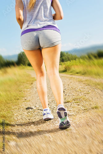 Young plus size fit woman running outdoors on sunny summer day. Rear view of female jogger in gray shorts, natural lighting, vibrant colors.