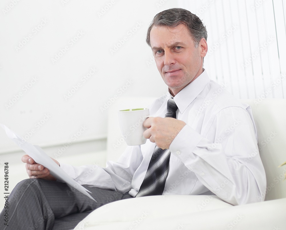 confident businessman drinking tea and reading a document,sitting in a chair in the hotel room confident businessman drinking tea and reading a document,sitting in a chair in the hotel room