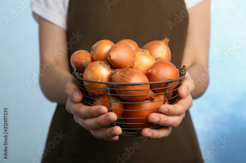 Woman holding basket with ripe onions on color background