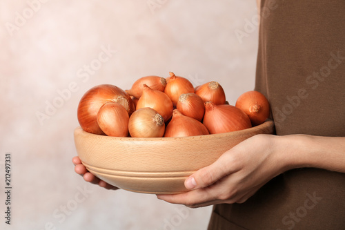 Woman holding bowl with ripe onions on grey background