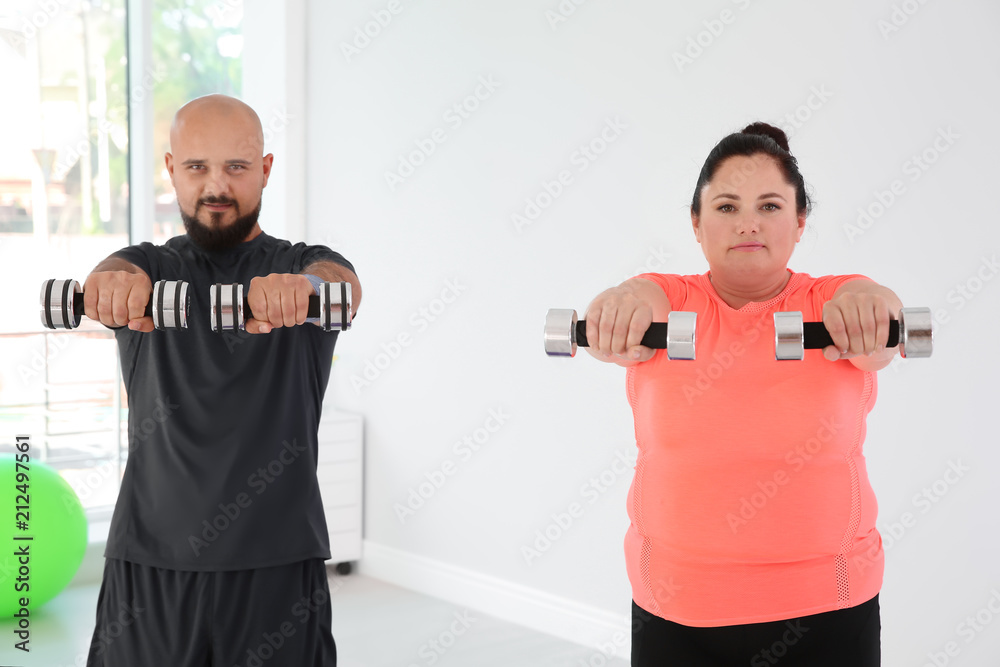 Overweight man and woman doing exercise with dumbbells in gym Overweight man and woman doing exercise with dumbbells in gym