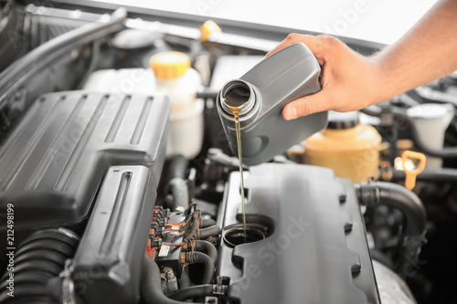 Mechanic pouring oil into car engine, closeup