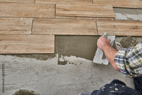 Hands of the tiler are laying the ceramic wood effect tiles on the floor