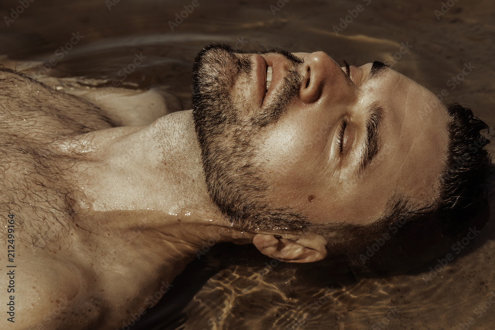 Strong face male model on the nature background with sand and water on the beach on the sunset Strong face male model on the nature background with sand and water on the beach on the sunset