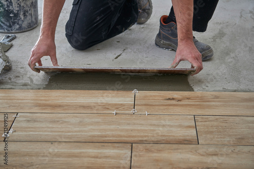 Hands of the tiler are laying the ceramic wood effect tiles on the floor