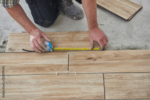 Laying wood effect tiles on the floor. Worker laying floor tiles.