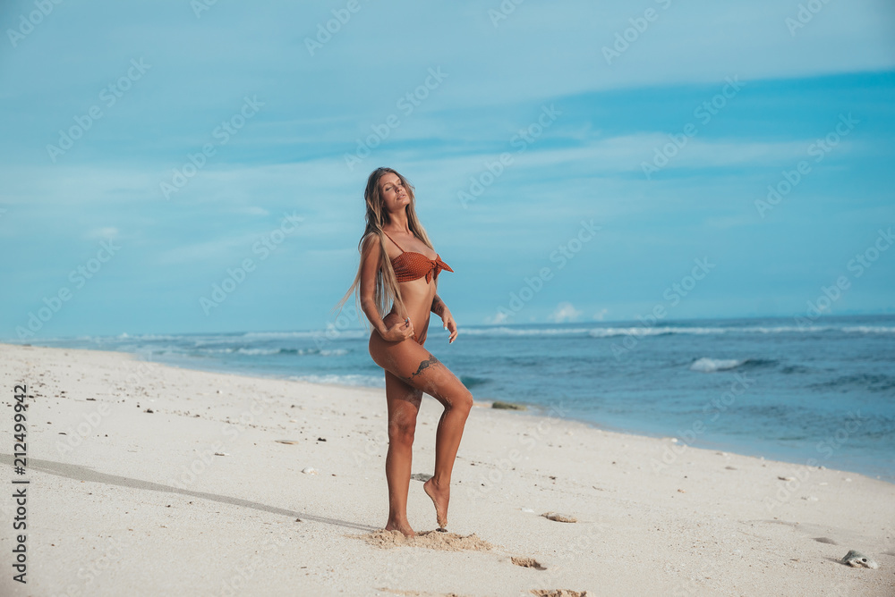 A tall, thin model with an elegant figure posing on a white empty beach, puts the round ass back, throws his head up to the sun, enjoys the wind and the noise of the water.