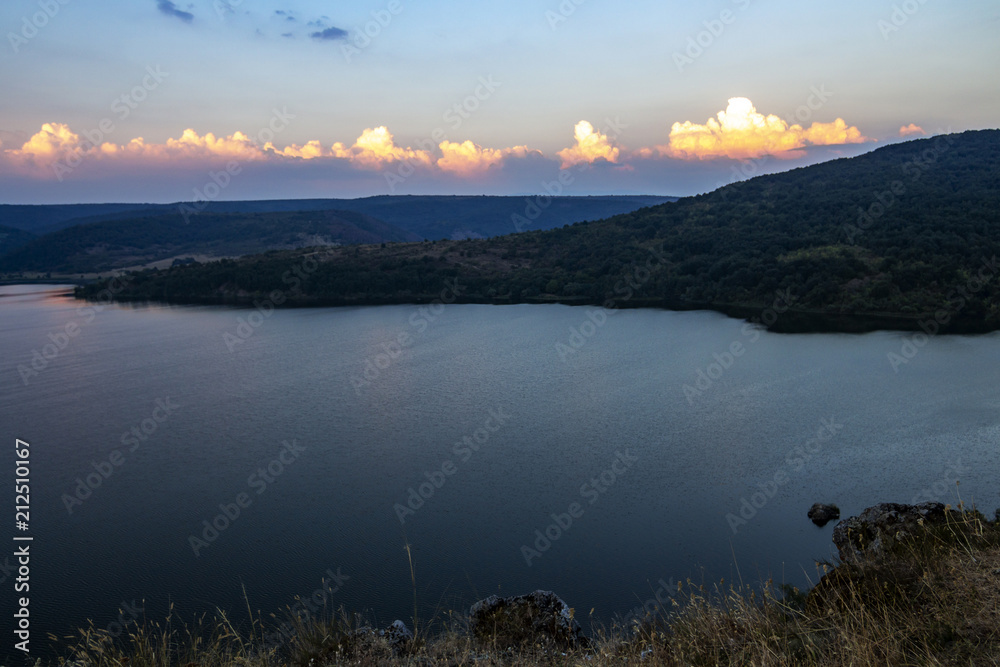 August sunset view to Pchelina Dam, Bulgaria with a row of sunlit clouds from the rocks next to the medieval non-functional Church of St. John Letni