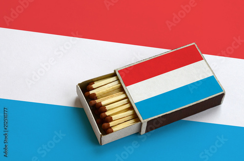 Luxembourg flag  is shown in an open matchbox, which is filled with matches and lies on a large flag photo