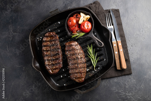 Closeup ready to eat steak Top Blade beef breeds of black Angus with grill tomato, garlic and on a wooden Board. The finished dish for dinner on a dark stone background. Top view