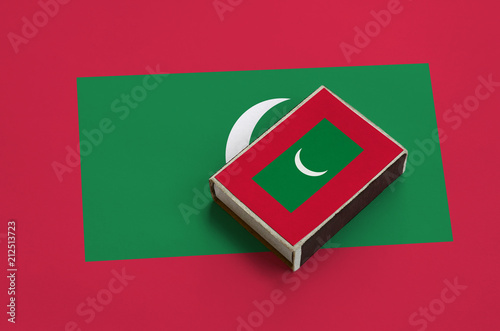 Maldives flag  is pictured on a matchbox that lies on a large flag photo