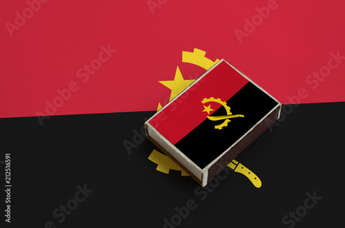 Angola flag  is pictured on a matchbox that lies on a large flag photo