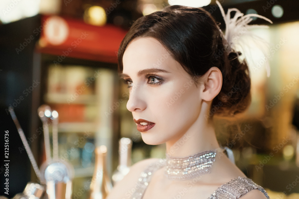 Naklejka premium Close-up portrait of a young attractive woman in a 1920s style at the bar. Model with a beautiful make-up