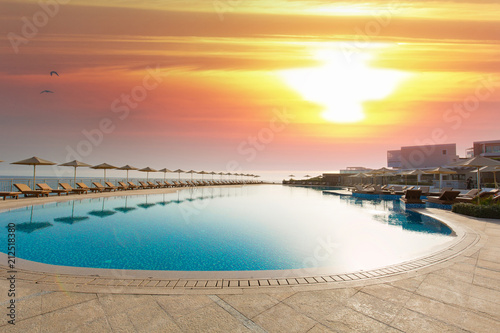 Hotel swimming pool, outdoor, with sunbeds around, sunset