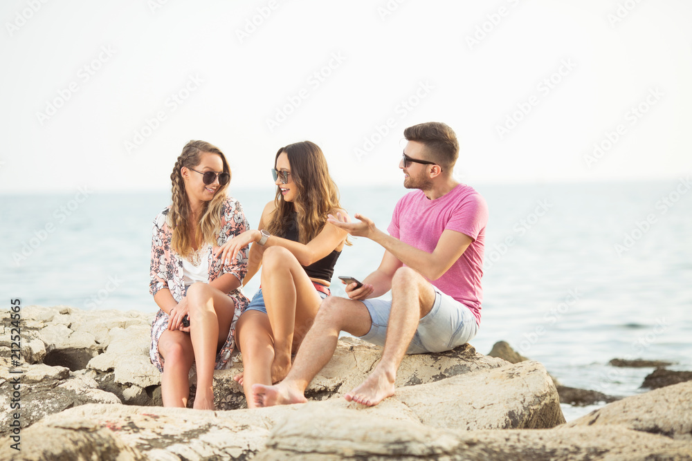 Thre young friends sitting on rocks near sea Thre young friends sitting on rocks near sea