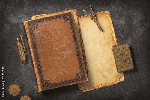 Steampunk / Gaslight themed mockup with a vintage book, a stack of grungy paper and antique brass items on a dark metal background photo