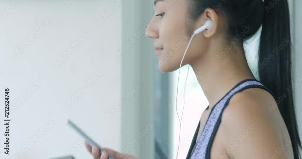 Attractive asian girl running on the treadmill in the gym with earphones, to keep fit and be toned or lose weight.