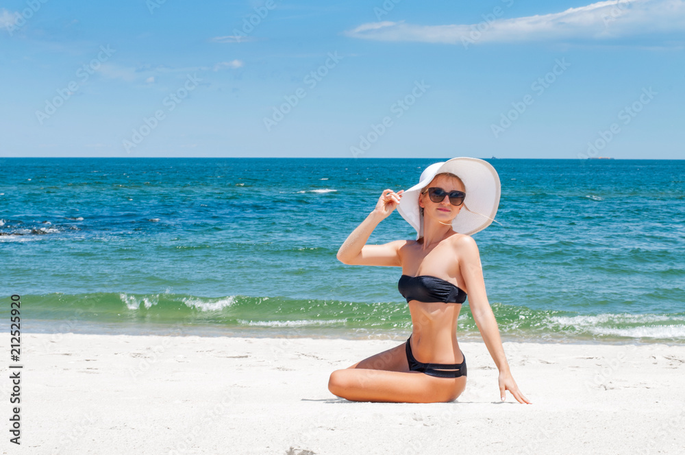 Beautiful woman in bikini and hat sitting on the beach Beautiful woman in bikini and hat sitting on the beach