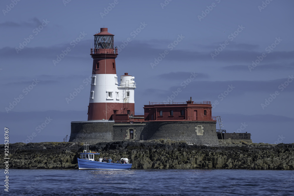 Longstone Lighthouse located in the Farne Islands of the United Kingdom with blue boat in front of it
