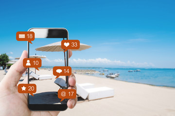 Hand mobile smart phone at the beach in summer, and social media with social network notification icons