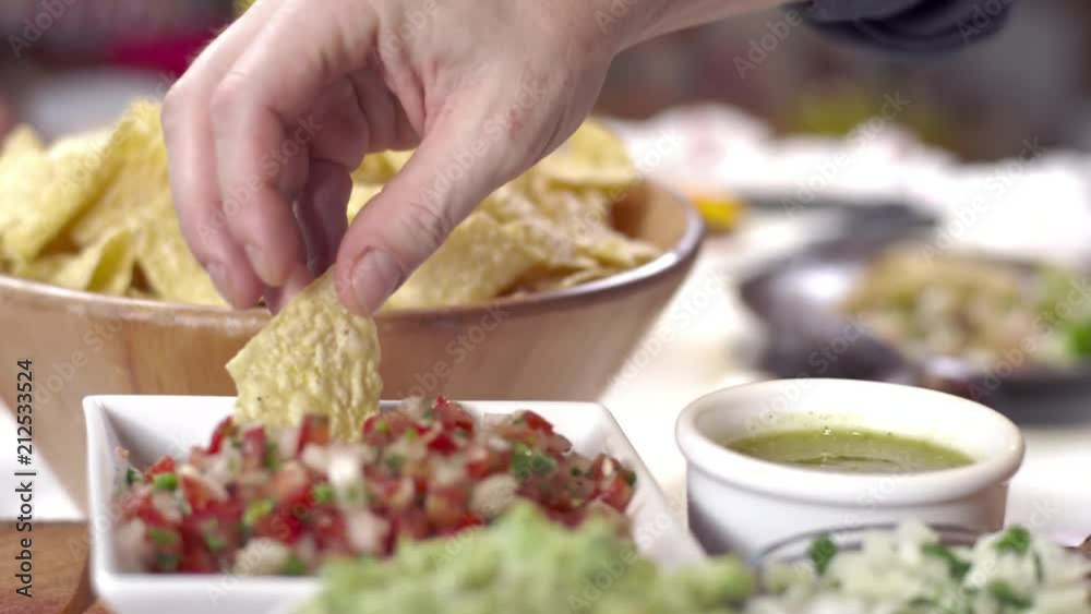 Dolly shot of hand picking up tortilla chip and dipping into salsa Dolly shot of hand picking up tortilla chip and dipping into salsa