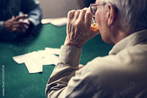 A senior man drinking alcohol in a cards circle