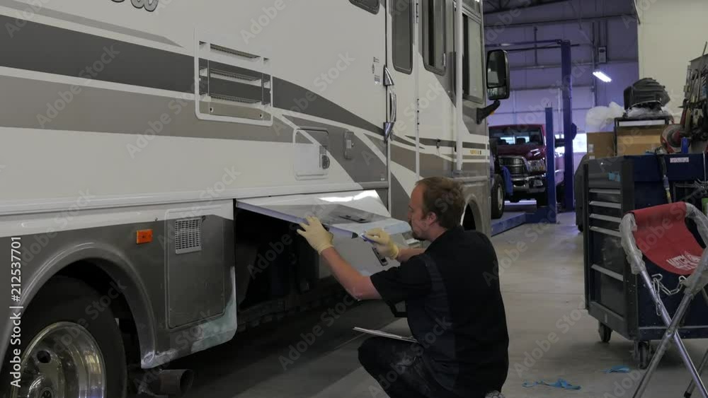 Man repairing a large RV in a body shop. Man repairing a large RV in a body shop.