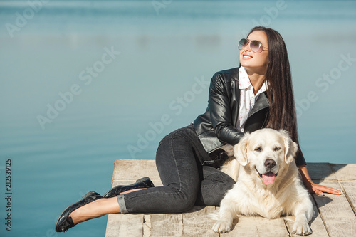 Young attractive woman sitting at the pier with her dog. Best friends outdoors