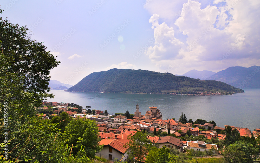 Monte Isola island inside Iseo Lake, green hill covered by forests, surrounded by water, sunny summer day