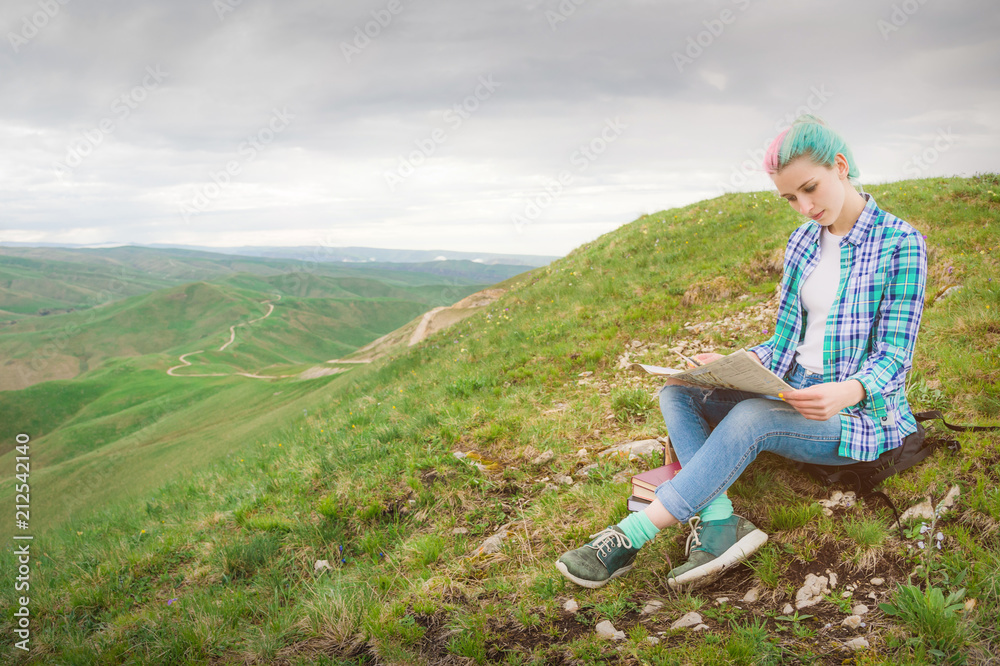 Girl traveler with multi-colored hair sitting on nature reading card and holding a compass in hand. The concept of navigating the search and tourism in the mountains. Travel Concept