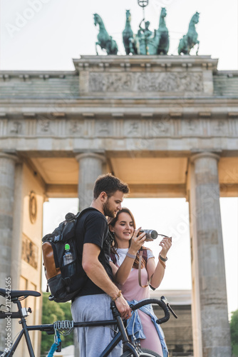 Photography couple of tourists with backpacks and bicycle looking at photo camera in front o