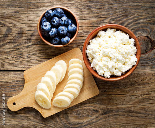 Brown wooden Bowl of homemade curd with banana, jam, blueberries on a dark brown wooden background, top view, copy space photo