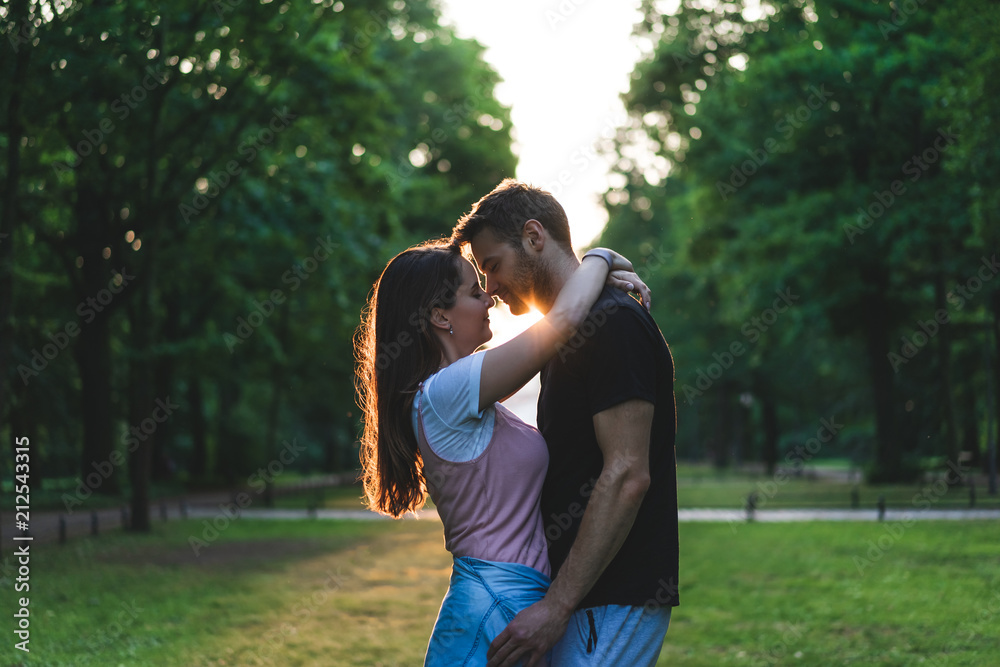 side view of woman embracing boyfriend and kissing him on meadow in park side view of woman embracing boyfriend and kissing him on meadow in park