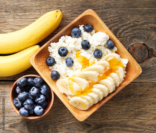 Brown wooden Bowl of homemade curd with banana, jam, blueberries on a dark brown wooden background, top view, copy space photo