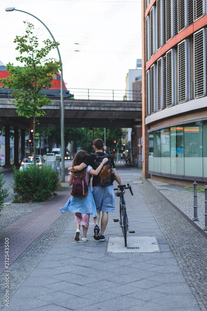 rear view of couple of tourists with backpacks and bicycle walking at street of Berlin, Germany