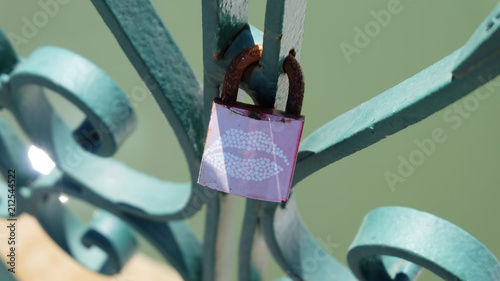 A love lock with a kiss mark, chained onto the metal rail of a bridge. A love lock or love padlock which sweethearts lock to a bridge, fence, gate, or monument, to symbolize their love.
