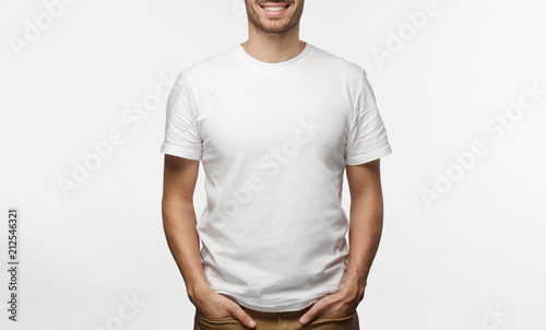 Handsome man in white tshirt isolated on grey background, smiling, standing in hands in pockets pose