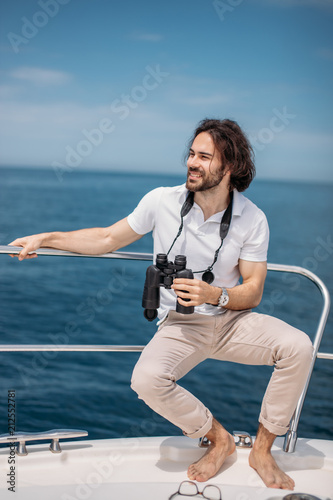 Caucasian Bearded Traveller Man looking through binoculars from the boat, adoring beauty and power of the Ocean photo