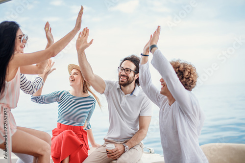 Group of friends, dressed in casual cloth, giving high five on a fashionable yacht - Happy people having a fancy party on a luxury boat