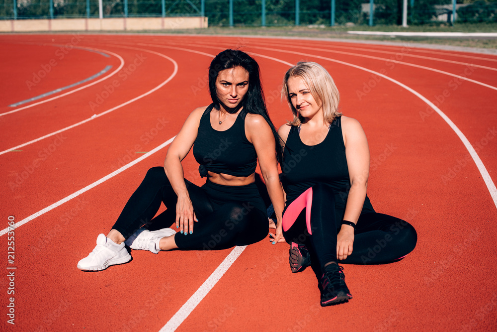 Chubby woman and trainer sit on cover of athletics stadium