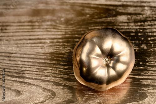 Gold painted tomato on golden and wooden background.