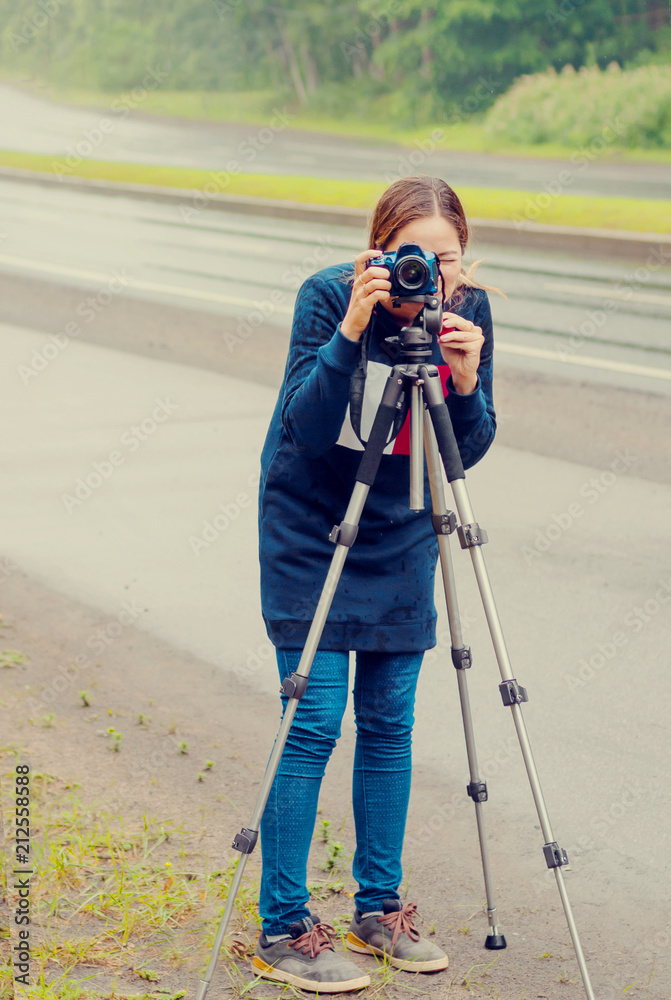 Freelance photographer shooting lifestyle. Girl taking pictures on a road near woods.
