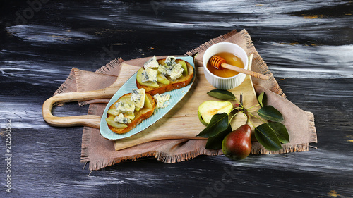 Sweet bruschetta with pears, cheese and honey on the whole grain roasted bread - on wooden background, close up, selective focus. Natural daylight photo