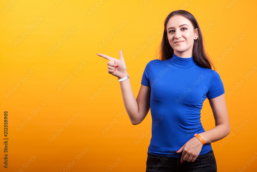 Smilling pretty woman pointing away over yellow background Smilling pretty woman pointing away over yellow background